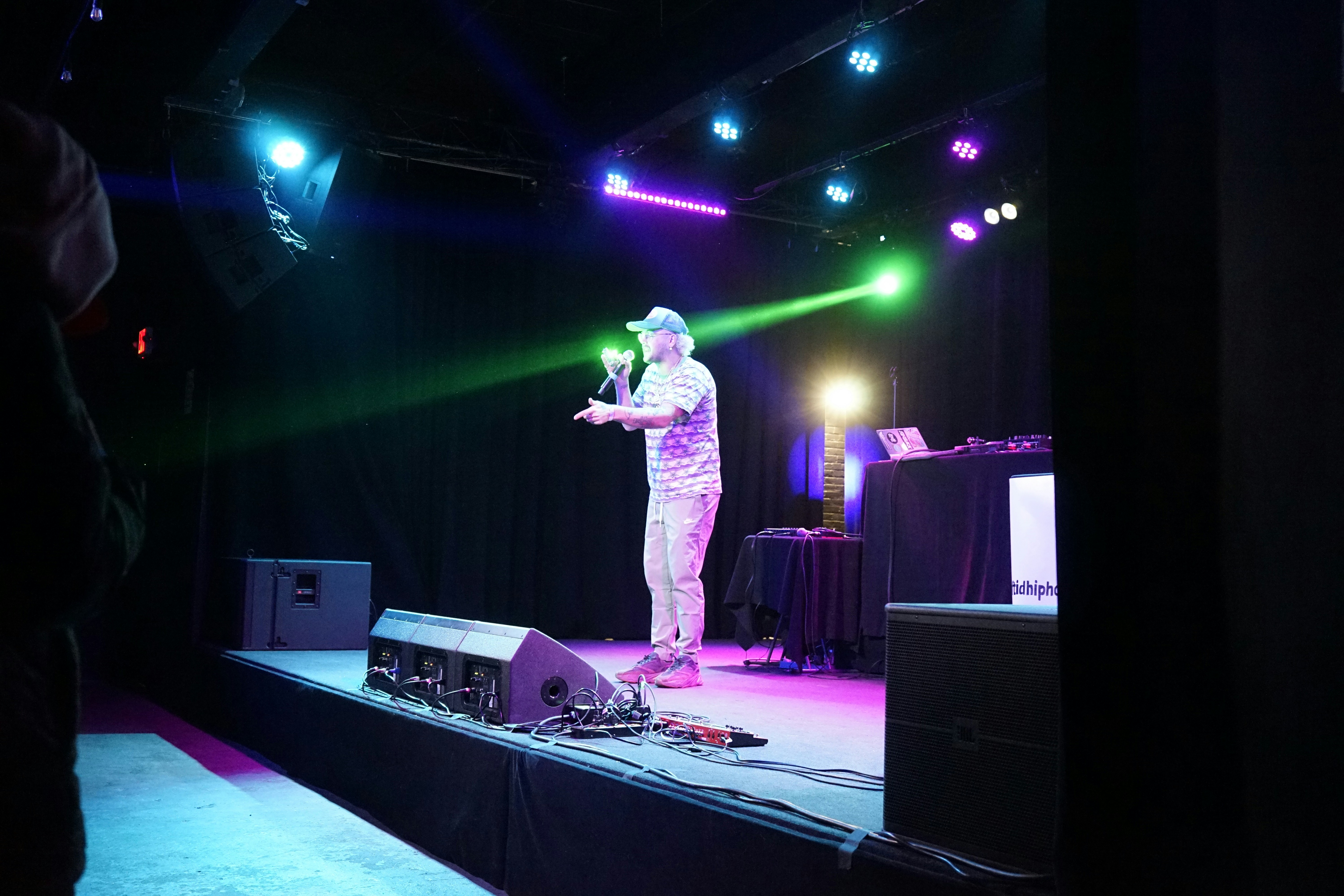 A man speaking on a stage with colorful lights.