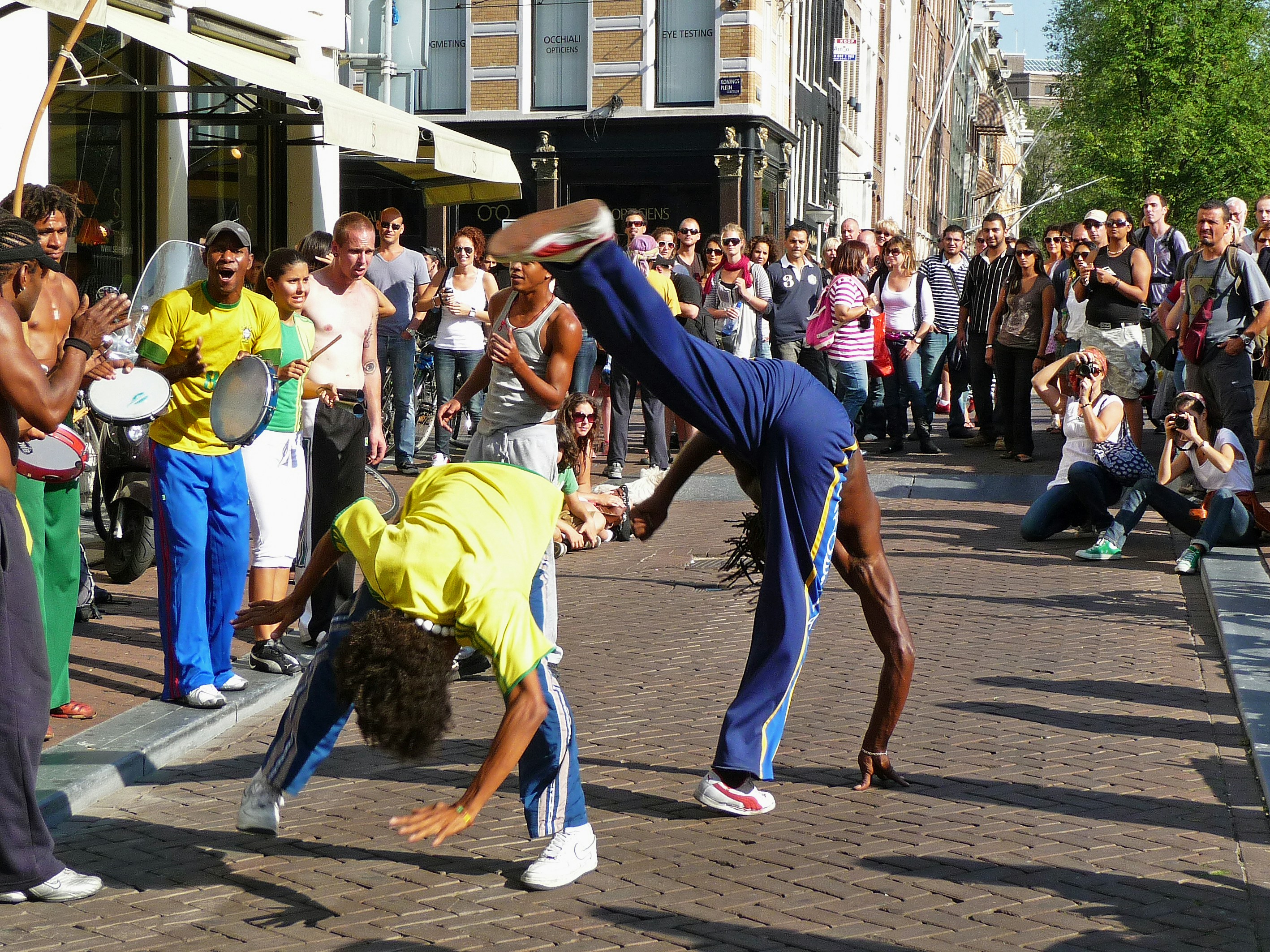 Street dance photo, Amsterdam city - a picture of breakdancers at the corner of square Koningsplein and canal Singel, in the old town. I enjoyed this spontaneous performance art with the other people. Only a few minutes,and two other dancers started to dance their turn. Other people of the group made the music and were singing at the left. And many people kept watching - nice public. Amsterdam city in free photos - urban photos of people in the streets, August 2009. Human street photography in The Netherlands by Fons Heijnsbroek. by Magic Trick people walking on street during daytime