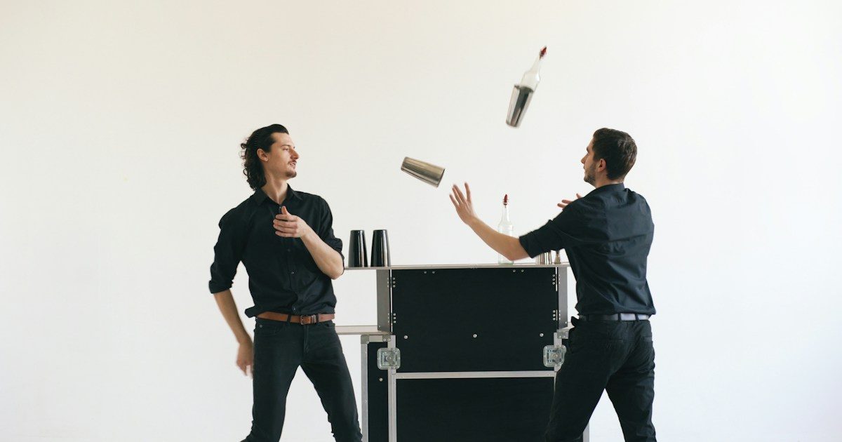 Professinal bartender men juggling bottles and shaking cocktail at mobile bar table on white background studio by Magic Trick Two bartenders juggling bottles and shakers