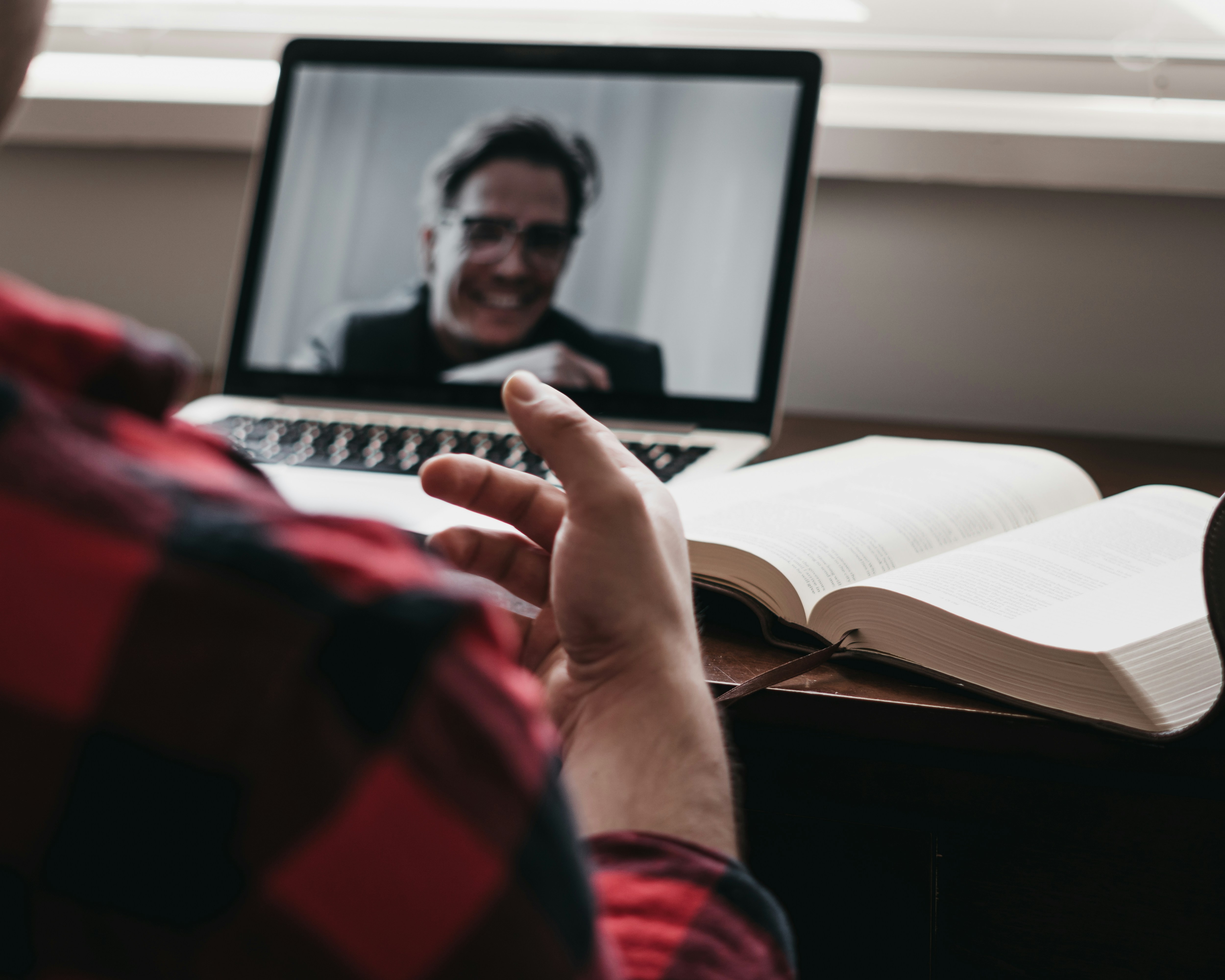 Online Video Call with Bible on Table by Magic Trick person in red and black plaid long sleeve shirt using black laptop computer