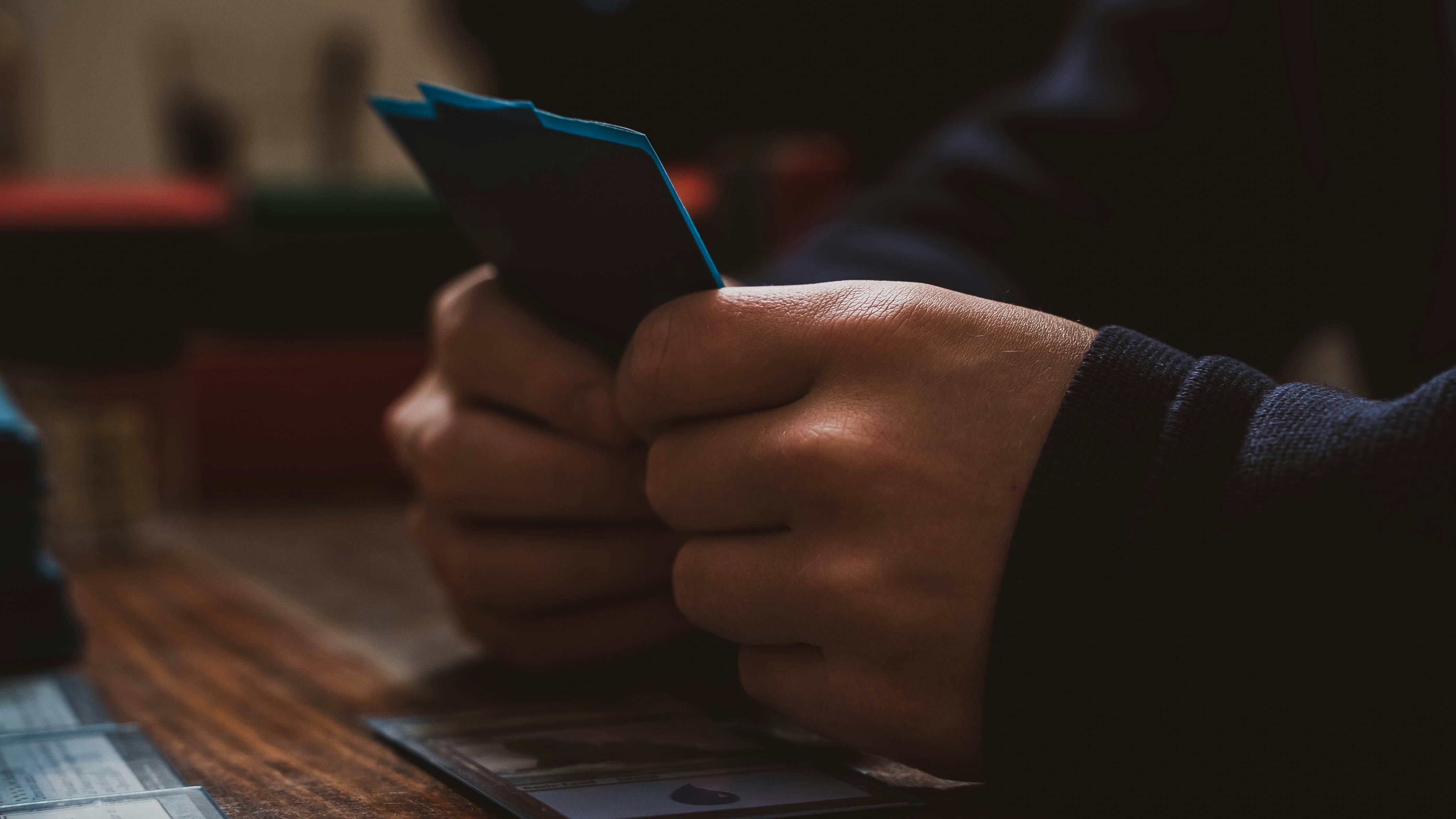 A gamer looks through a hand of trading cards. by Magic Trick a person sitting at a table using a cell phone